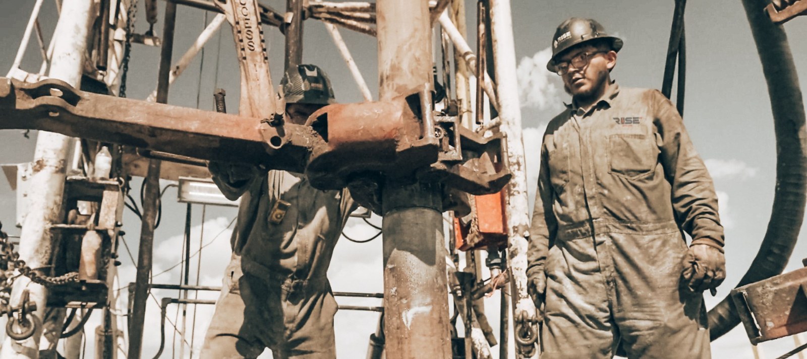 Rise Drilling crew members in coveralls and hard hats working the rig floor